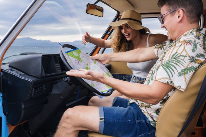 Touristic man exploring map with help of long haired woman in hat in front seat of car