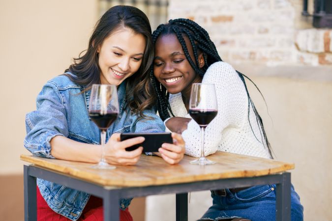 Female friends laughing at phone screen at a restaurant with red wine