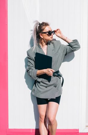 Stylish businesswoman with laptop leaning on wall