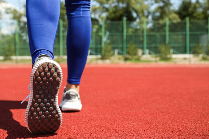 Girl walking on red athletic track, space for text