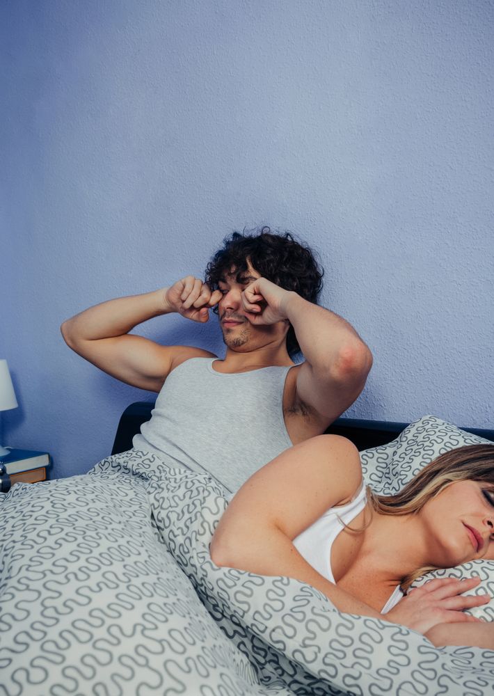 Man waking up and rubbing his eyes while his wife sleeps