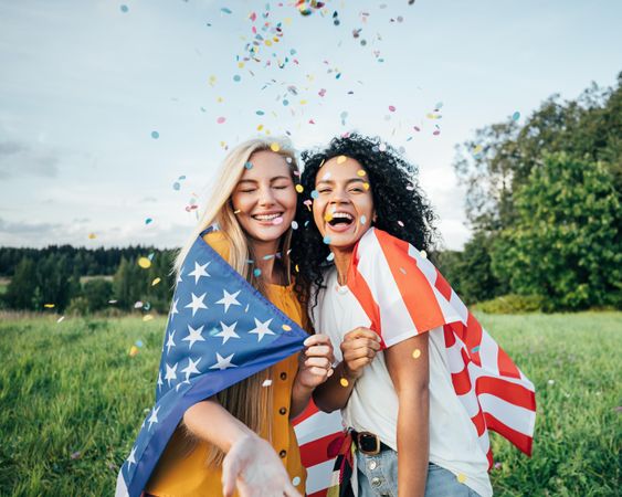 Two happy women covered by the USA flag with falling confetti