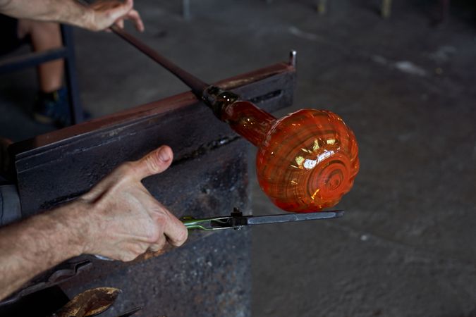 Crop gaffer shaping melted glass in dark workroom