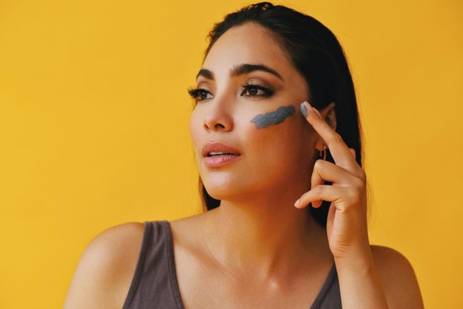 Latina woman looking away while applying clay mask with hand, copy space