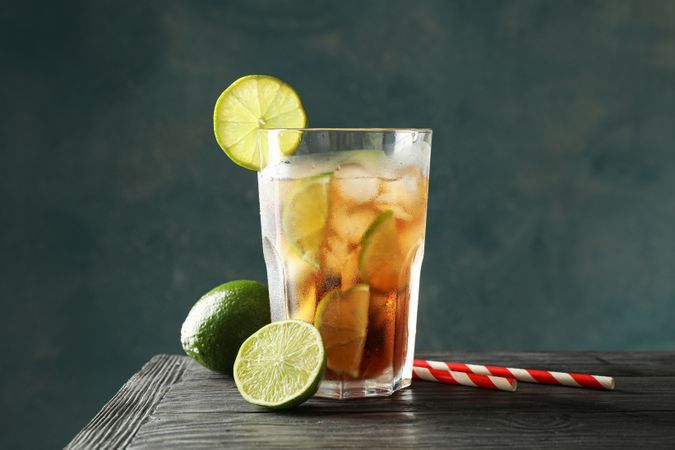 Glass of cold cola with citrus and ice on wooden table against dark background