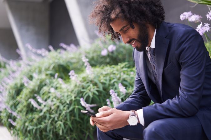 Joyful man in suit sitting outside and messaging