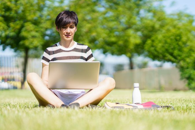 Woman sitting cross legged in park with computer and water bottle