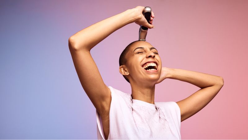 Cheerful female using a hair clipper on her head