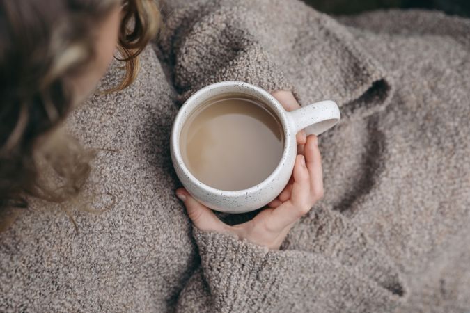 Woman in beige winter sweater holding ceramic spotted cup of coffee