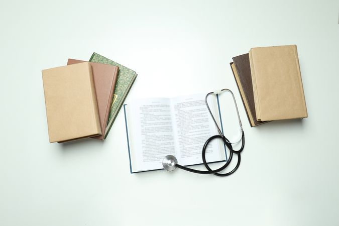 Books and stethoscope on light background, top view