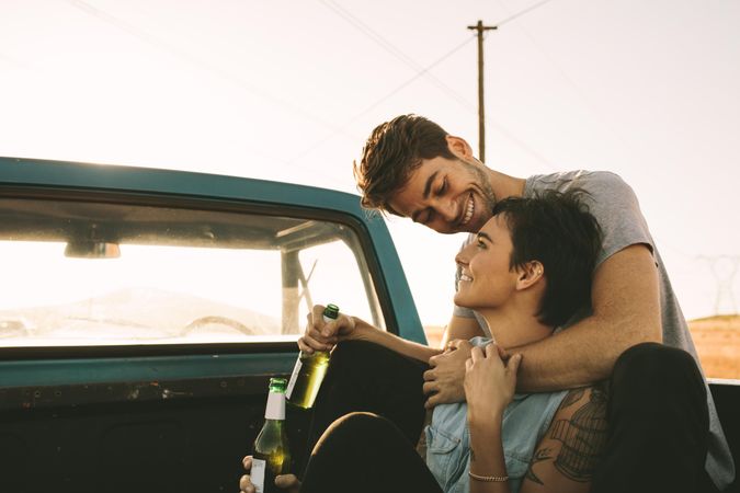 Happy couple enjoying bottled beverages in back of vintage truck