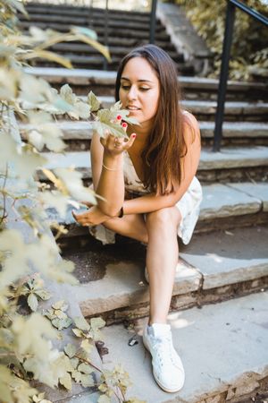 stylish woman sitting on stairs of park in New York smelling flowers