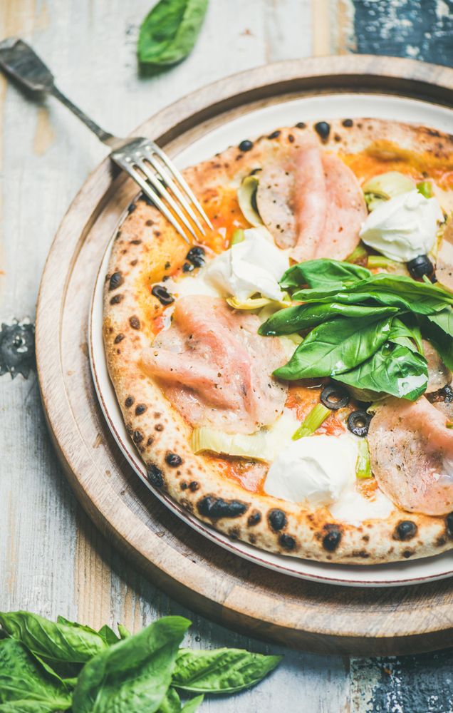 Freshly made wood fire oven pizza with spinach, ham and olives, close up, vertical composition