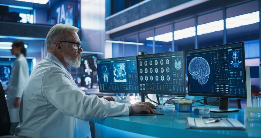 Male Neuroscientist Using Desktop Computer To Analyze MRI Scans Of Brain In Medical Research Center Laboratory.