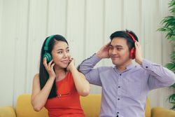 Male and female having fun listening to headphones on yellow couch