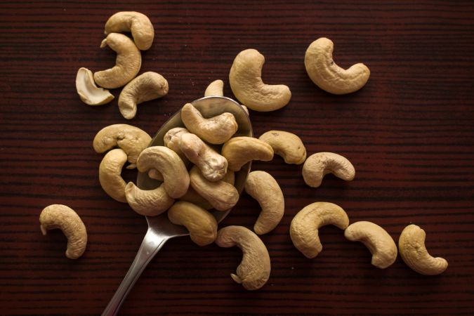 Top view of tasty cashew nuts placed on a steel spoon on a wooden background