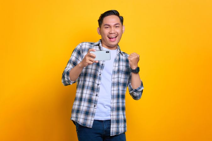 Smiling Asian male holding his phone and taking a photo with it