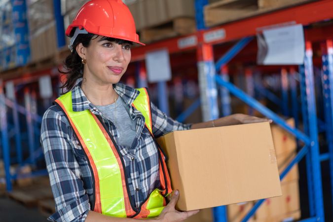Woman in hard hat carrying in box to be shipped at work