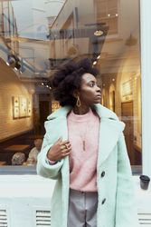Woman in turquoise coat standing on sidewalk looking away