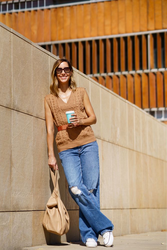 Smiling woman standing in sun with coffee and bag