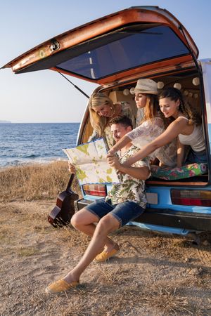 Puzzled man exploring map with help of long haired women in trunk of car
