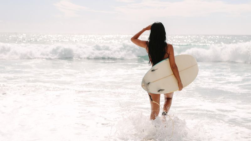 Slender surfer holding surfboard looking out for waves