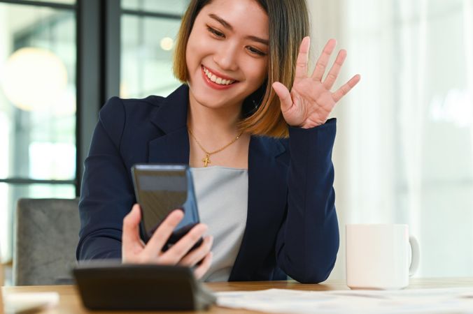 Asian woman in suit greeting friends with smartphone