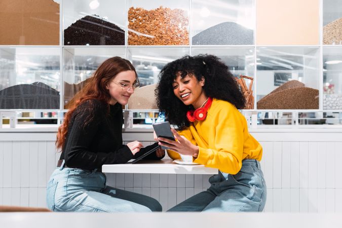 Positive multiethnic female friends using smartphones and laughing in cafe