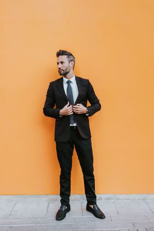 Adult stylish man in costume near orange wall