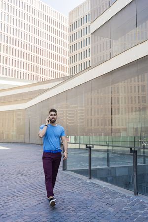 Cheerful modern businessman speaking on phone while walking outdoors