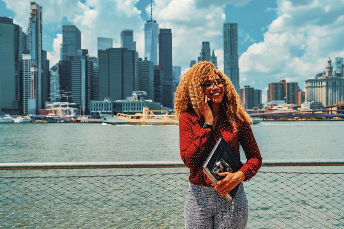 Happy professional Black female speaking on phone by Hudson River
