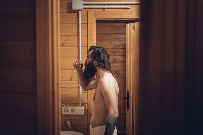 Bearded man brushing teeth in wooden house