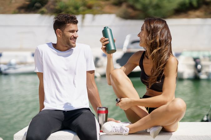 Man and woman sitting on pier with water bottles