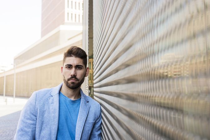 Young bearded man leaning on a wall and looking at camera