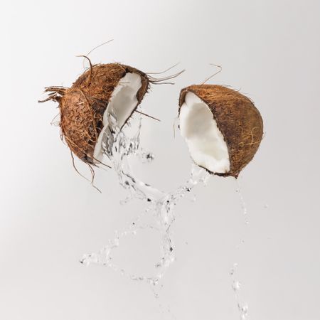 Cracked coconut with water splash on light background