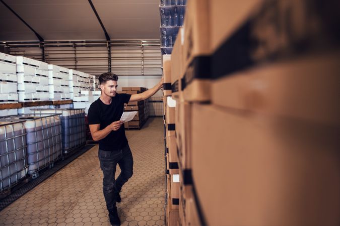 Young man tracking stock of packaged beer boxed in warehouse
