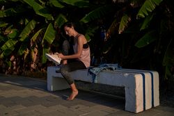 Hispanic woman putting on sneakers near plants