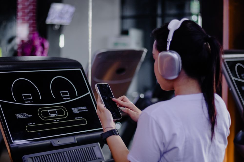 Asian woman using cellphone on treadmill for workout routine at gym