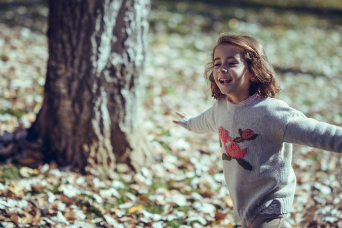 Joyful child running in park of colorful fall leaves with her arms open