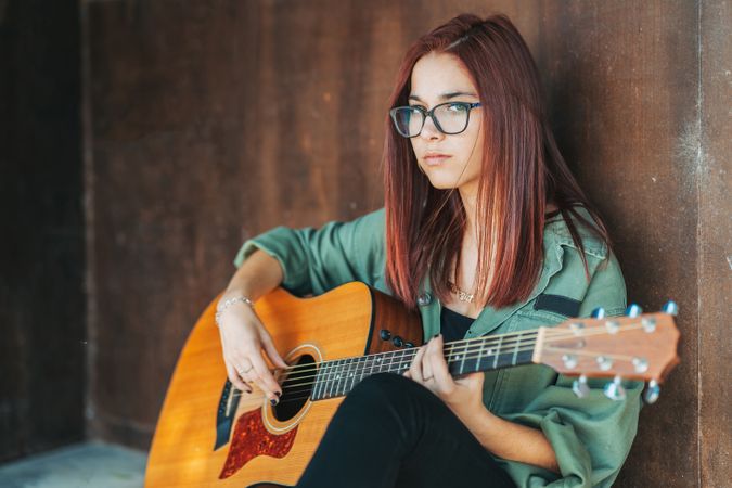 Romantic woman playing guitar leaning on wall