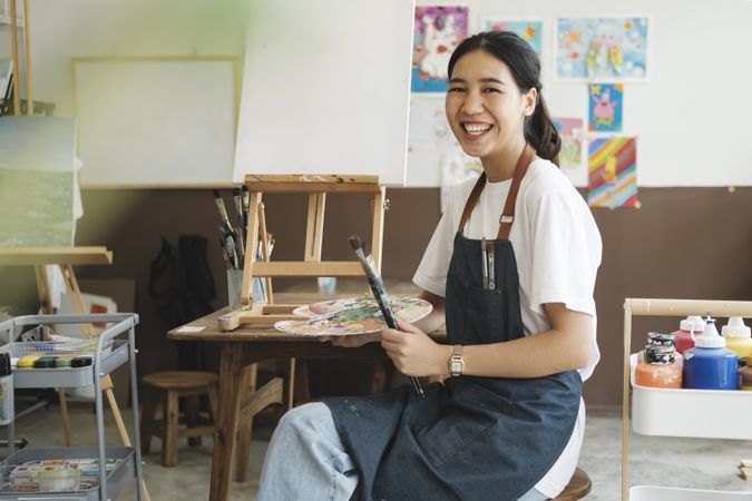 Young Asian female artist in art studio look at camera and smiling.