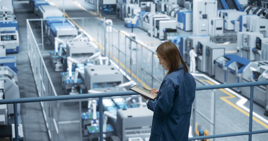 Portrait of a Japanese Engineer Using Tablet Computer and Looking Around a Factory Facility with Equipment Producing Modern Electronic Components for Different Industries