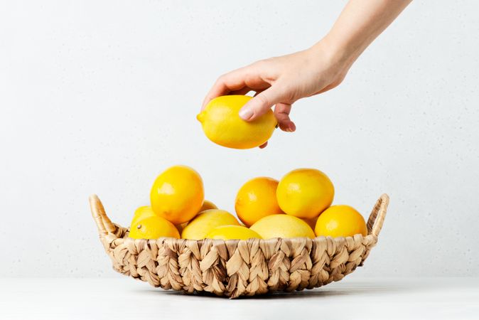 Hand grabbing a lemon of a pile in basket