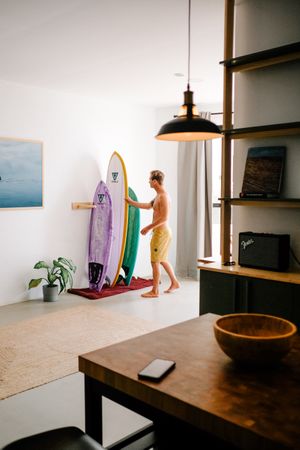 Man choosing surfboard from rack in home