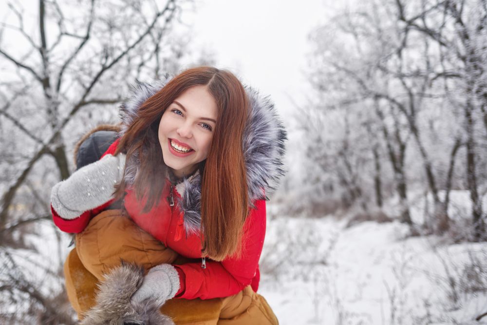 Teenage girl happy and hanging off other person’s shoulder in snowy forest