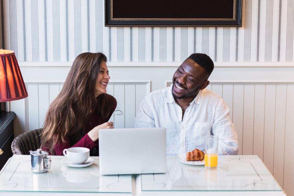Cheerful multiethnic couple using laptop during breakfast at home