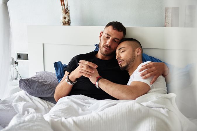 Smiling gay couple hugging on bed