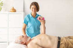 A female physical therapist helps rehabilitate the wrist and arm of an older man