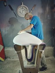 Serious tattooed surfboard shaper polishing surface in workshop
