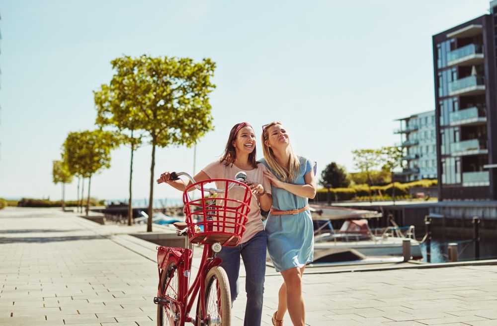 Two women smiling and walking with bicycle